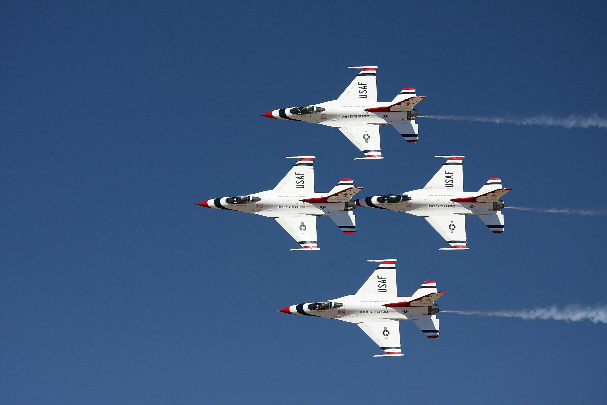Four USAF fighter jets performing an aerial maneuver against a clear blue sky.